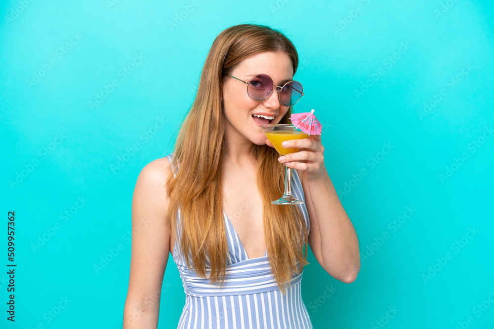 Young woman isolated on blue background in swimsuit and holding a cocktail Young woman isolated on blue background in swimsuit and holding a cocktail