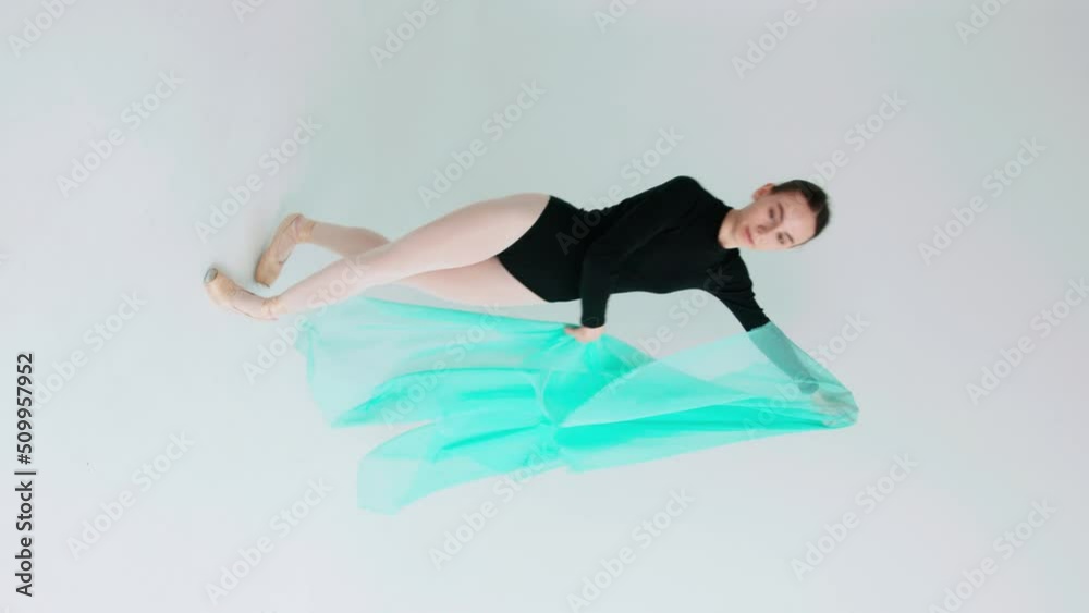 A ballerina in a black leotard performs a classical dance in a white studio with a fluttering turquoise veil in her hands. Vertical video A ballerina in a black leotard performs a classical dance in a white studio with a fluttering turquoise veil in her hands. Vertical video