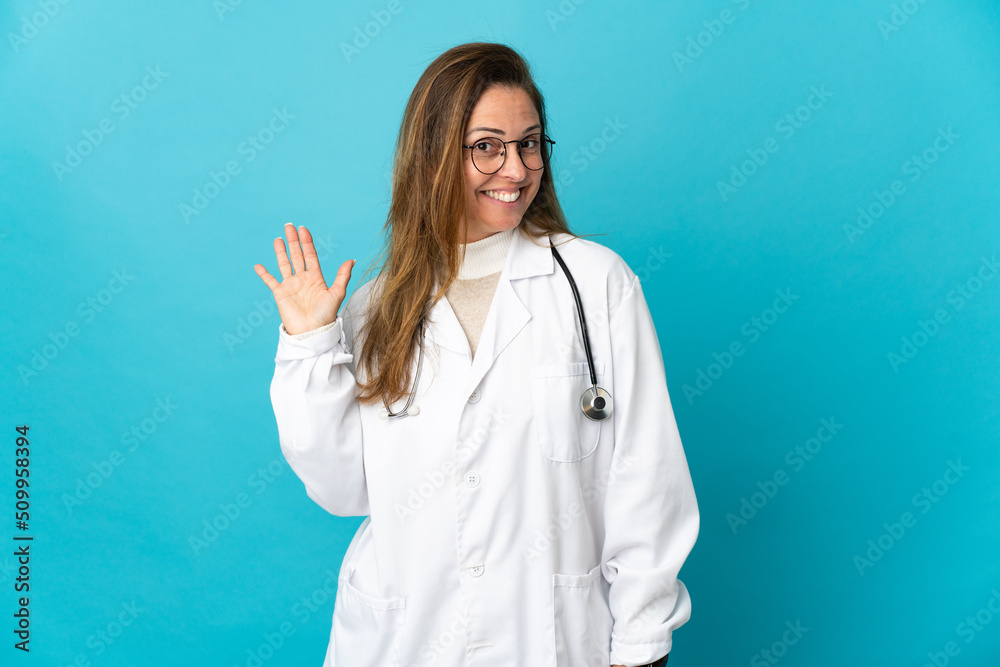Middle age Brazilian doctor woman isolated on blue background saluting with hand with happy expression Middle age Brazilian doctor woman isolated on blue background saluting with hand with happy expression