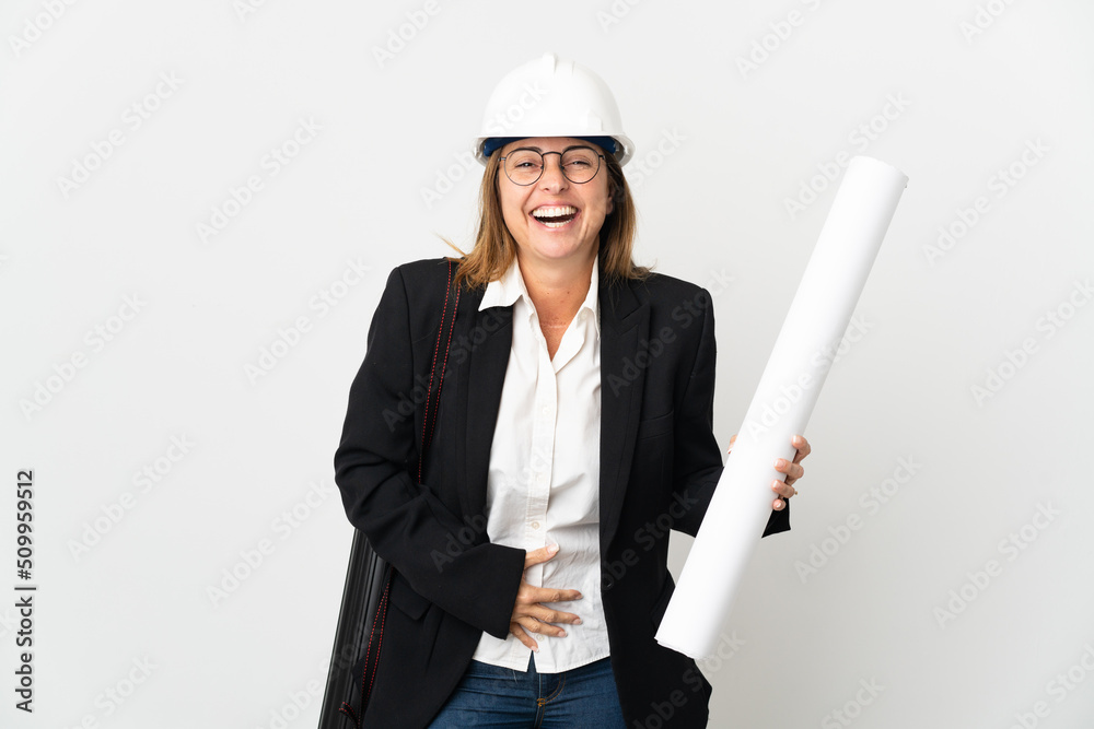 Middle age architect woman with helmet and holding blueprints over isolated background smiling a lot Middle age architect woman with helmet and holding blueprints over isolated background smiling a lot