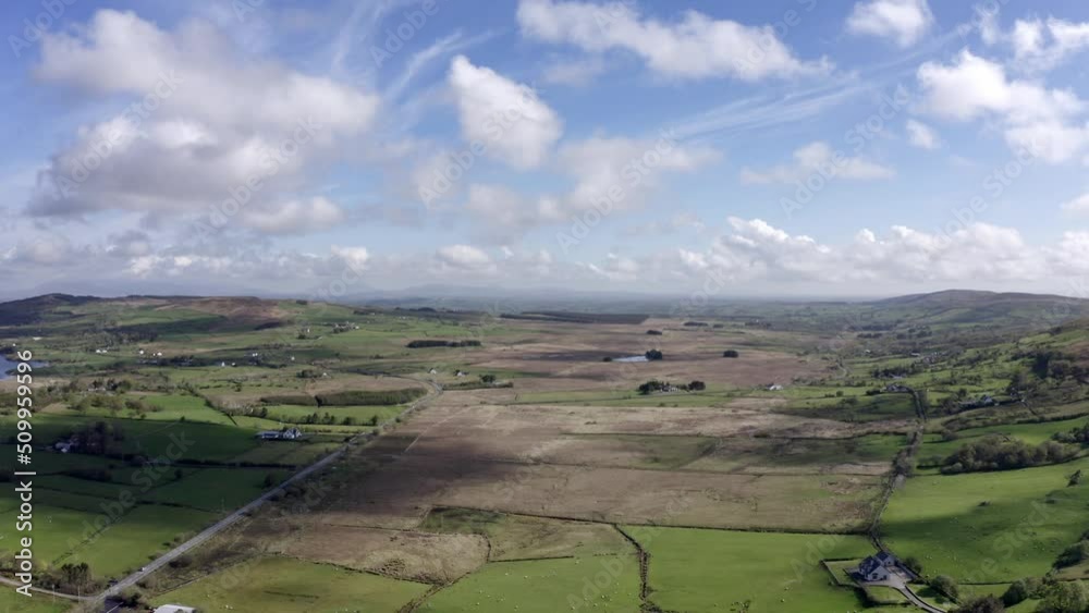 Aerial view of green farmland in Ireland. Irish rural landscape, panorama, little village, empty road, hills in the background Aerial view of green farmland in Ireland. Irish rural landscape, panorama, little village, empty road, hills in the background