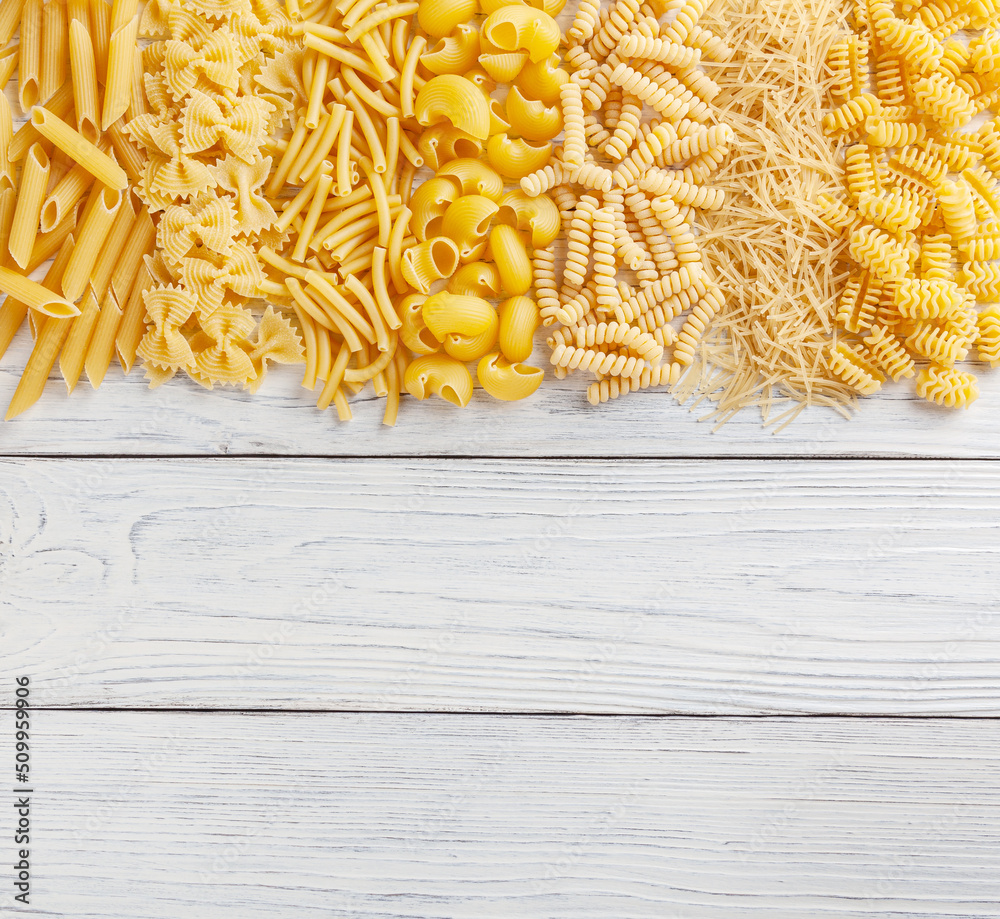 Different types and shapes of Italian pasta on white wooden background