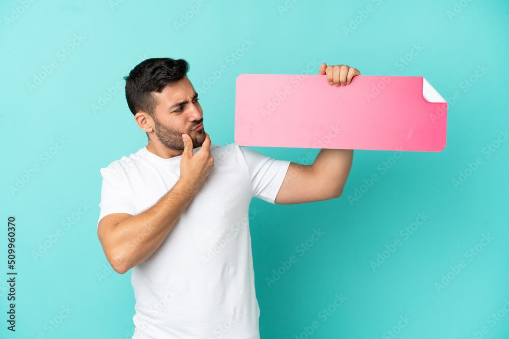 Young handsome caucasian man isolated on blue background holding an empty placard and thinking Young handsome caucasian man isolated on blue background holding an empty placard and thinking