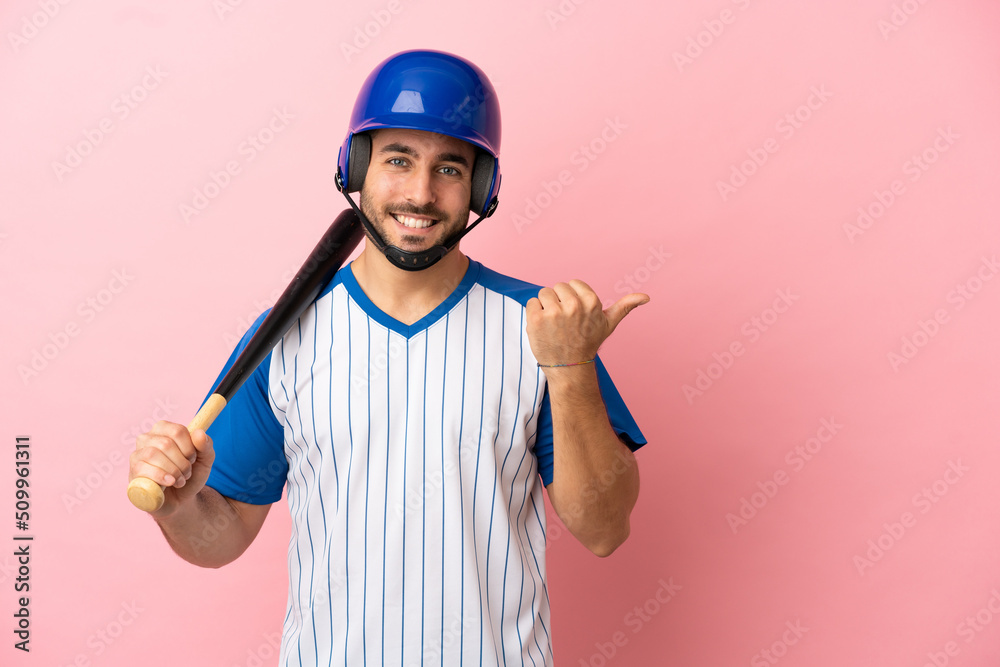 Baseball player with helmet and bat isolated on pink background pointing to the side to present a product Baseball player with helmet and bat isolated on pink background pointing to the side to present a product