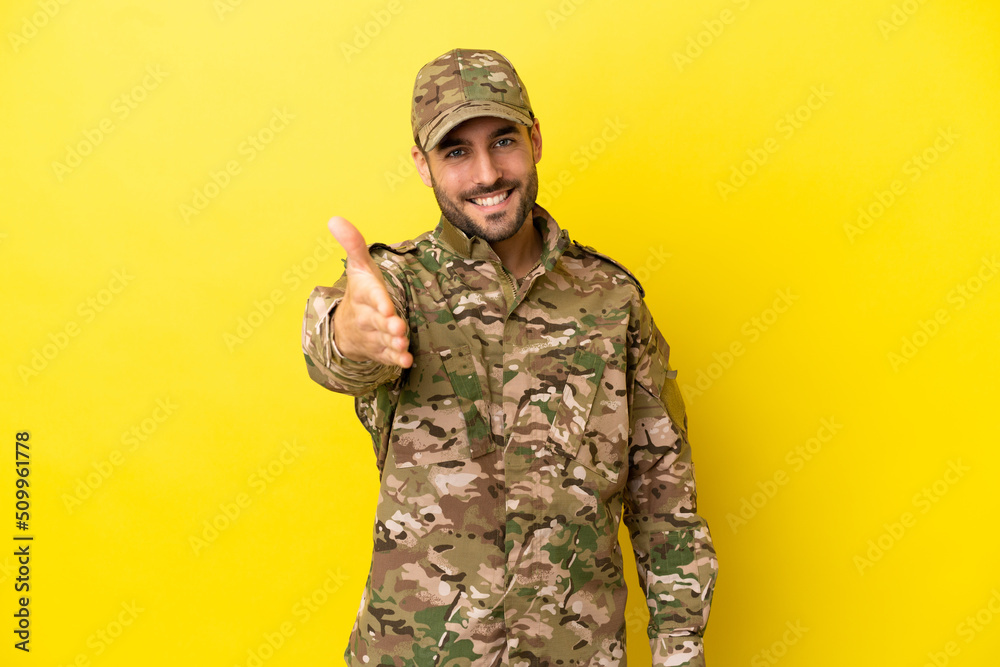 Military man isolated on yellow background shaking hands for closing a good deal Military man isolated on yellow background shaking hands for closing a good deal