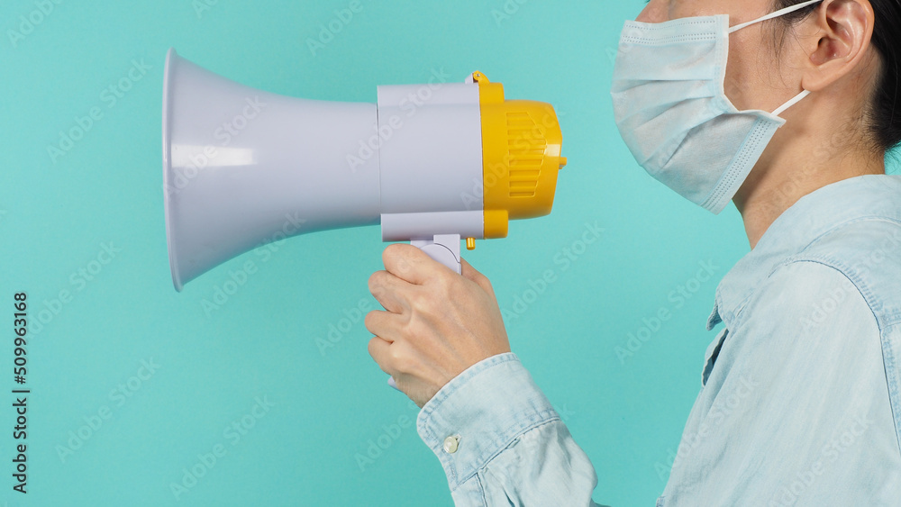 Asian woman hold megaphone and wear face mask on green mint background Asian woman hold megaphone and wear face mask on green mint background