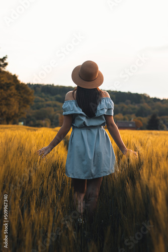 Breathtaking candid portrait of a brunette aged 20-24 walks in a beautiful blue dress and hat in a cornfield, smiling naturally. Fashion vintage style. Natural beauty of a brown haired European woman