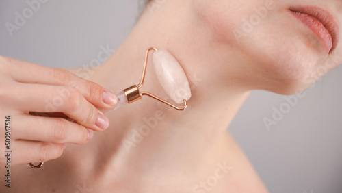 Close-up portrait of a woman using a quartz roller massager for an alternative fight against wrinkles on her neck. Smoothing of the rings of venus. 