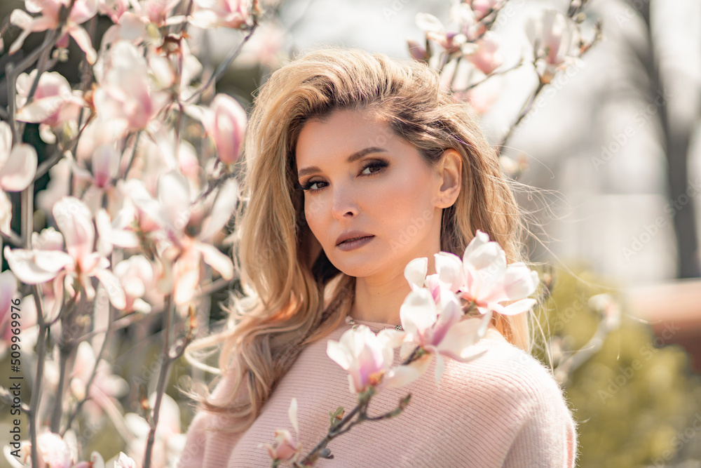 Portrait of a beautiful happy middle aged woman enjoying the smell in a blooming spring garden. Beautiful magnolia bushes, large flowers.