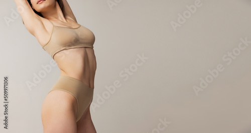 Leinwand Poster Cropped image of slim female body in beige underwear isolated over grey studio background