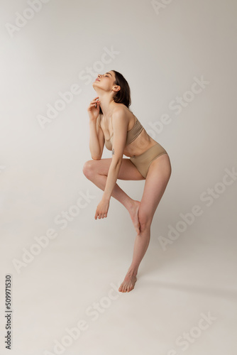 Portrait of beautiful young woman posing in beige underwear isolated over grey studio background