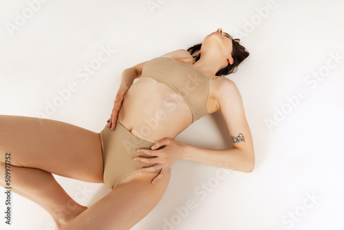 Portrait of young beautiful woman, lying on floor, posing in underwear isolated over grey studio background. Sensuality