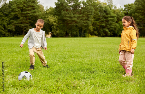 childhood, leisure games and people concept - happy little boy and girl with ball playing soccer at summer park