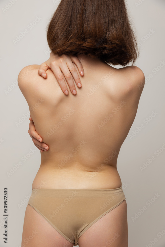 Cropped image of young slim woman posing in underwear isolated over grey studio background. Image of female back Cropped image of young slim woman posing in underwear isolated over grey studio background. Image of female back