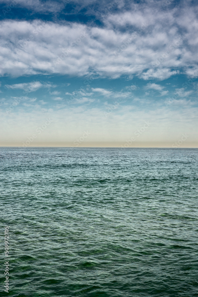 The surface of the sea under a cloudy blue sky. Blue wave surface of the sea going to the horizon.
