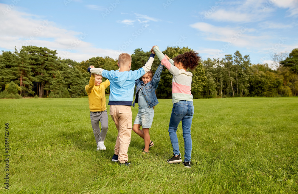 childhood, leisure and people concept - group of happy kids playing round dance at park