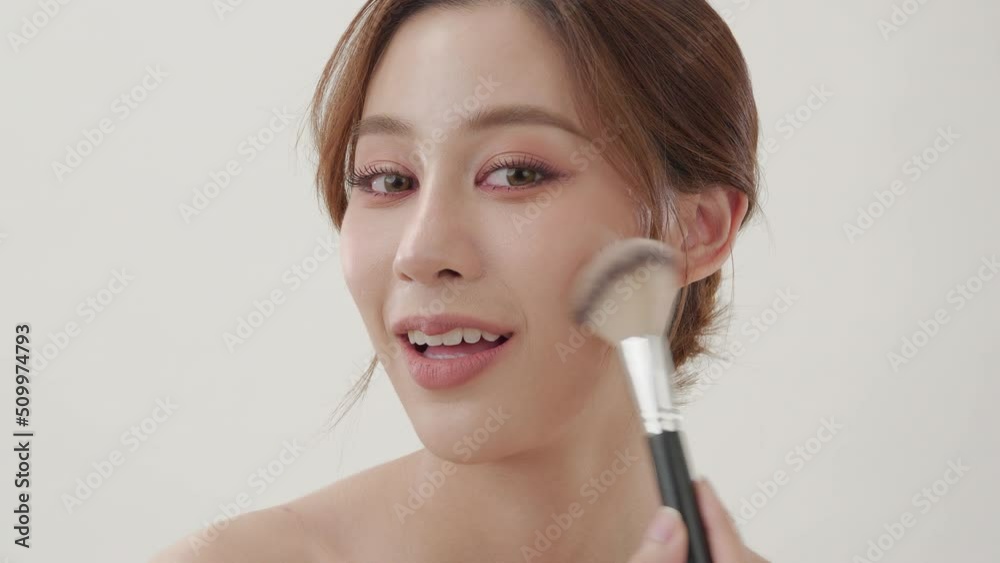 Young asian woman with beauty concept. Portrait of young beautiful lady posing at white background. She using blush powder to her face and looking to camera. Young asian woman with beauty concept. Portrait of young beautiful lady posing at white background. She using blush powder to her face and looking to camera.