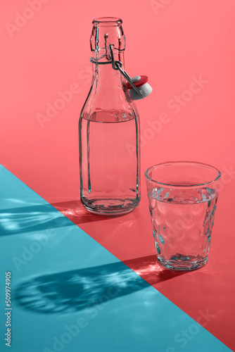 Obraz na płótnie Vintage bottles and glass with sun light shadows or reflection on pink-blue background. w salonie