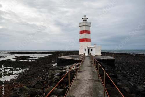 Scenic view of the old Garðskagi lighthouse in Garður under a cloudy sky, Reykjanes Peninsula, Iceland. Built in 1897, the old lighthouse with square ground plan is about 12.5 meters high.