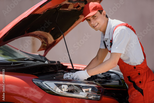 Car mechanic in red overall is repairing a car engine using a wrench..