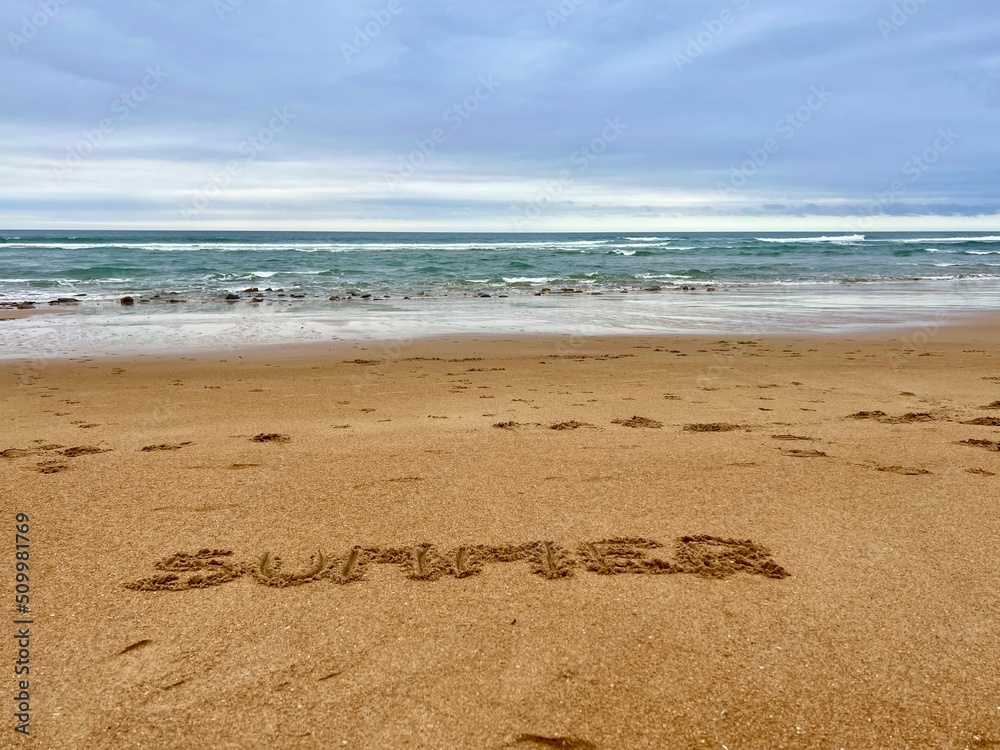 Word Summer handwritten on sandy beach with soft ocean wave on background Word Summer handwritten on sandy beach with soft ocean wave on background