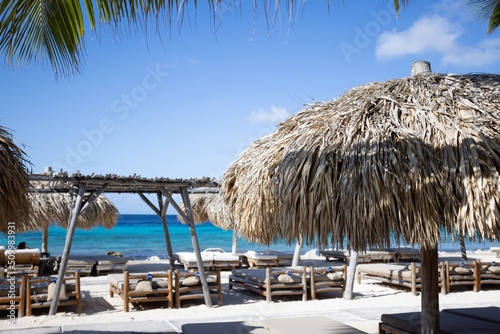 Wooden sun loungers with sun umbrellas on a tropical beach. Beach club.