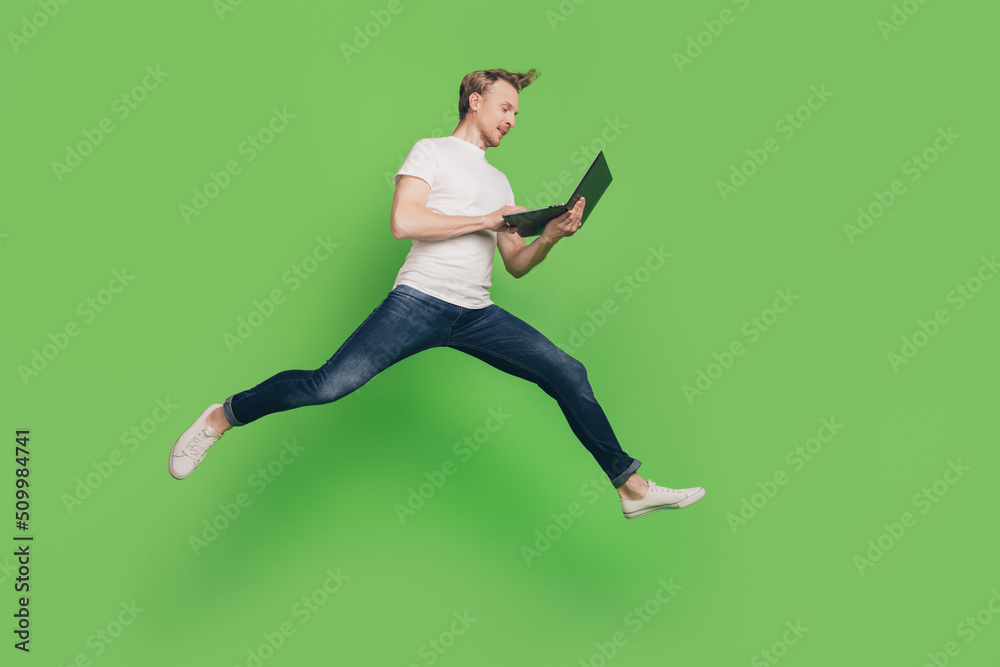 Profile photo of positive man hold computer jump run texting email wear white t-shirt on green color background Profile photo of positive man hold computer jump run texting email wear white t-shirt on green color background