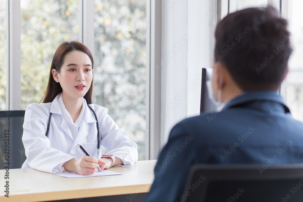 Fototapeta premium Asian professional woman doctor who wears medical coat talks with a man patient to consult and suggest healthcare information to him at the examination room in the hospital.