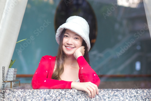 Beautiful Asian woman wears a white hat and red shirt while she sitting near glassed window in New Year and winter theme.