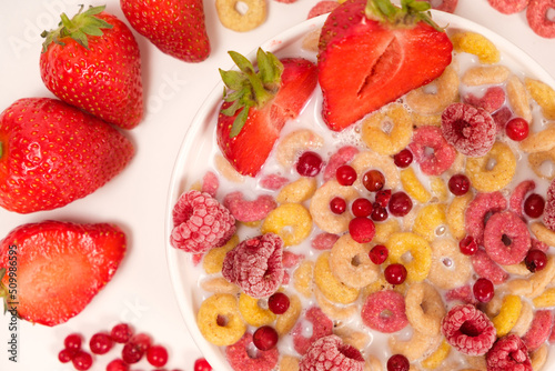 Fototapeta Naklejka Na Ścianę i Meble -  Corn rings with milk in a plate with berries and fruits, viewed from above on a white background. The concept of quick breakfast cereals