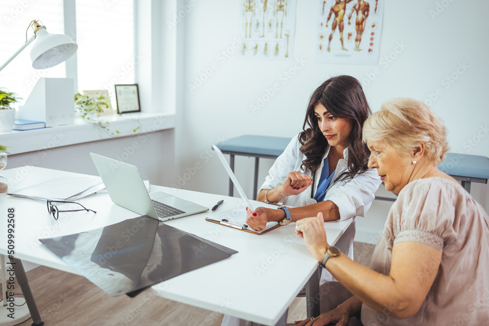 Fototapeta premium Patient Having Consultation With Female Doctor In Office. Smiling female patient at consultation with woman doctor sitting at table in office clinic.