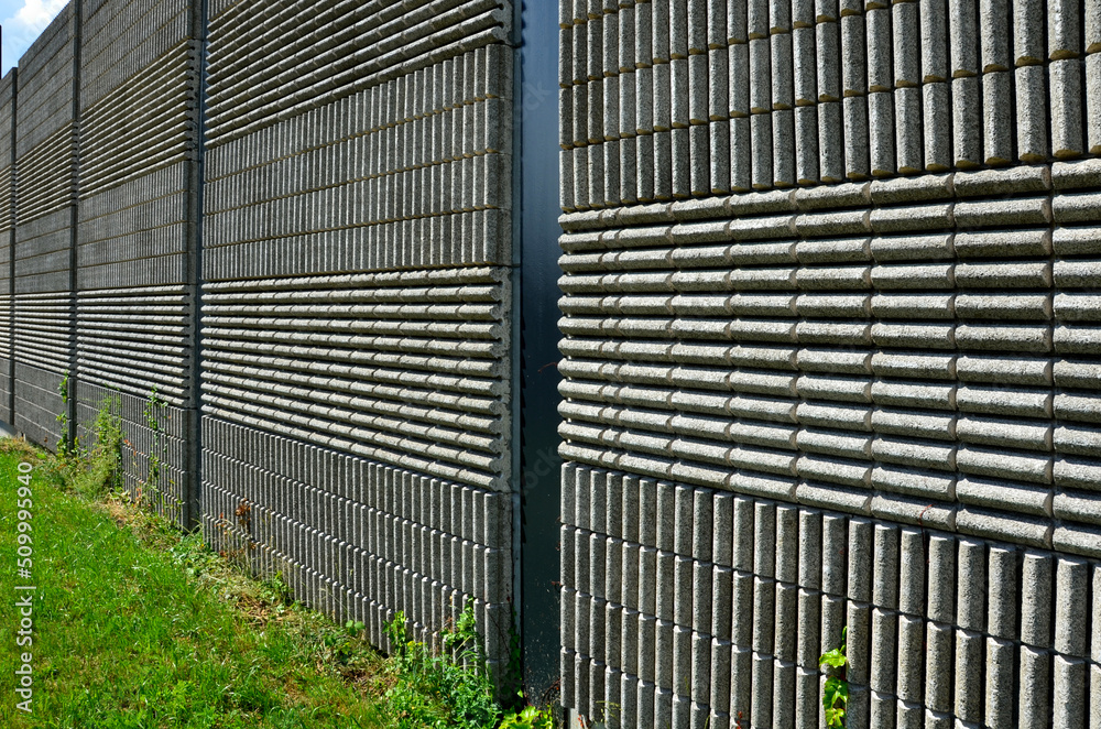 soundproof wall made of concrete porous ribbed material. fence of brown blocks inserted into metal beams, on the street. noise from road traffic does not get into the garden and residential area.
