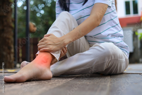 A young Asian woman sits down in a park holding her ankle due to pain in her ankle and grabs her sore ankle and flexes his leg while in severe pain. Exercise Injury Concept. exercise accident.