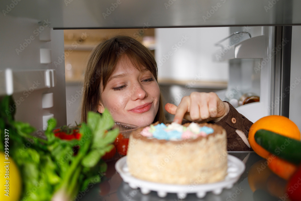 Girl tasting cake with finger in fridge Girl tasting cake with finger in fridge