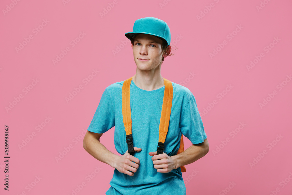 portrait of a guy in a blue t-shirt and cap stands with an orange backpack on a pink background portrait of a guy in a blue t-shirt and cap stands with an orange backpack on a pink background