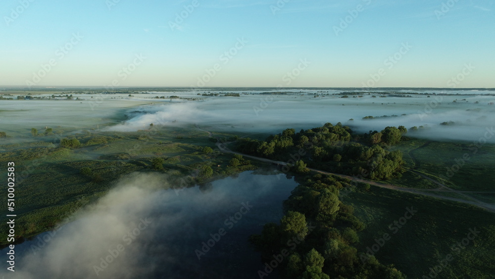 Bird's eye view of the mist over the river and meadows on an early summer morning