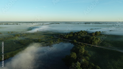 Bird's eye view of the mist over the river and meadows on an early summer morning
