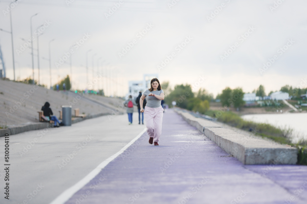 Overweight European teenage girl in tracksuit warms up, runs on violet floor concrete embankment, Sports and teenagers, overweight teenagers. Jogging helps the body to be strong.