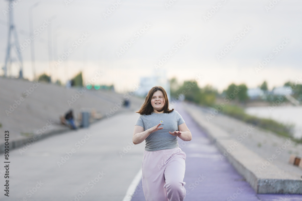 Overweight European teenage girl in tracksuit warms up, runs on violet floor concrete embankment, Sports and teenagers, overweight teenagers. Jogging helps the body to be strong.