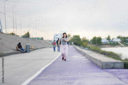 Overweight European teenage girl in tracksuit warms up  runs on violet floor concrete embankment  Sports and teenagers  overweight teenagers. Jogging helps the body to be strong.