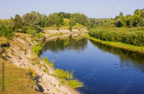 a small river with green and steep bank on a summer day 