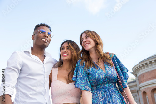multiracial group of three young friends hugging and walking enjoying a walk.