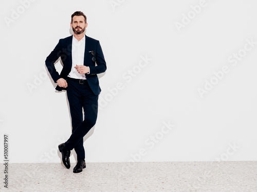 Portrait of handsome smiling stylish hipster lambersexual model. Sexy modern man dressed in black elegant suit. Fashion male posing in studio near white wall. Full length