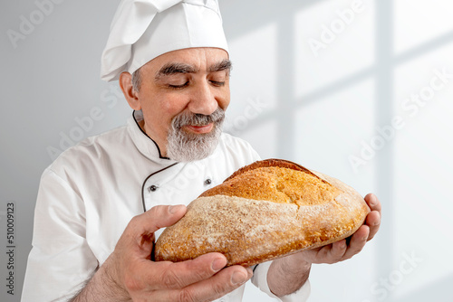 Professional baker quality checker smell the scent freshly baked bread. Chef-cooker in a chef's hat and jacket. Senior baker man wearing a chef's outfit. Character kitchener, pastry chef