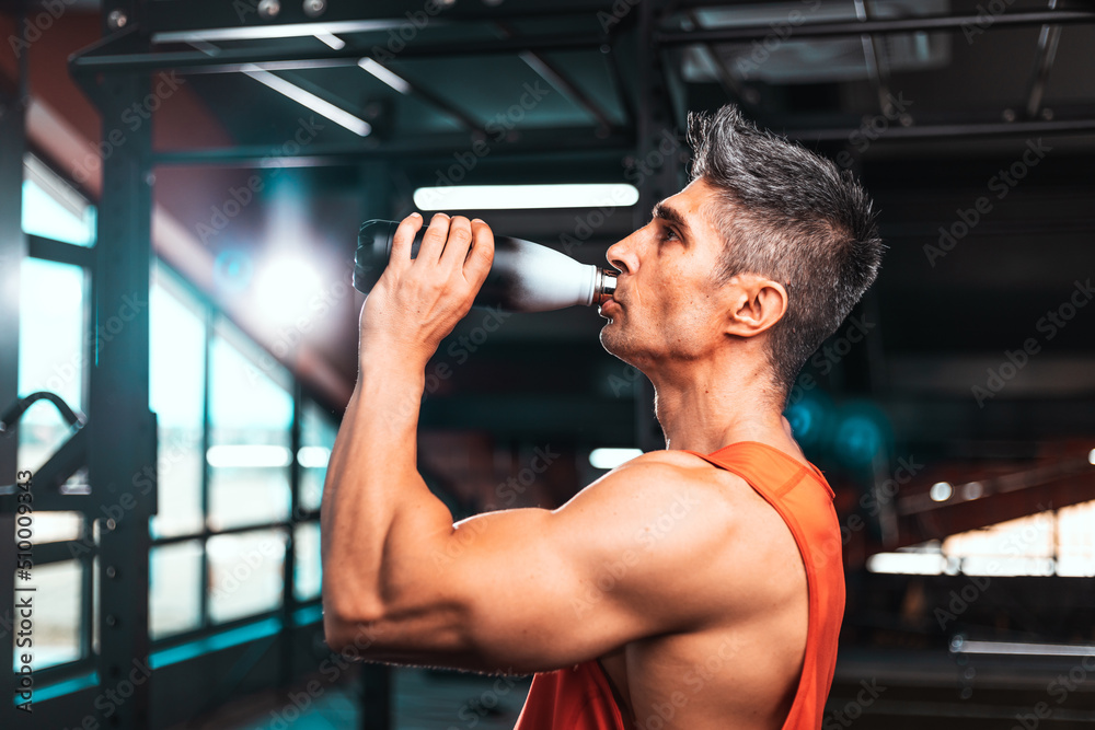 Lifestyle portrait of handsome muscular man drinking water in the gym. Middle aged man drinks water in the gym.