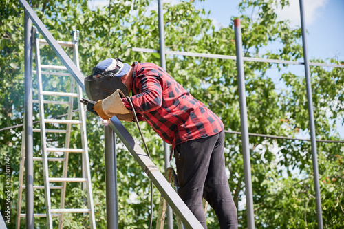 Wallpaper Mural Man welding metal pole with welding machine for installing solar panels. Welder working on sunny day at field in protective welding helmet. Metal pipes and trees on background. Green energy Torontodigital.ca