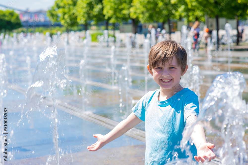 Naklejka premium happy child plays in a dry fountain. joyful smiling boy stands wet in the fountain