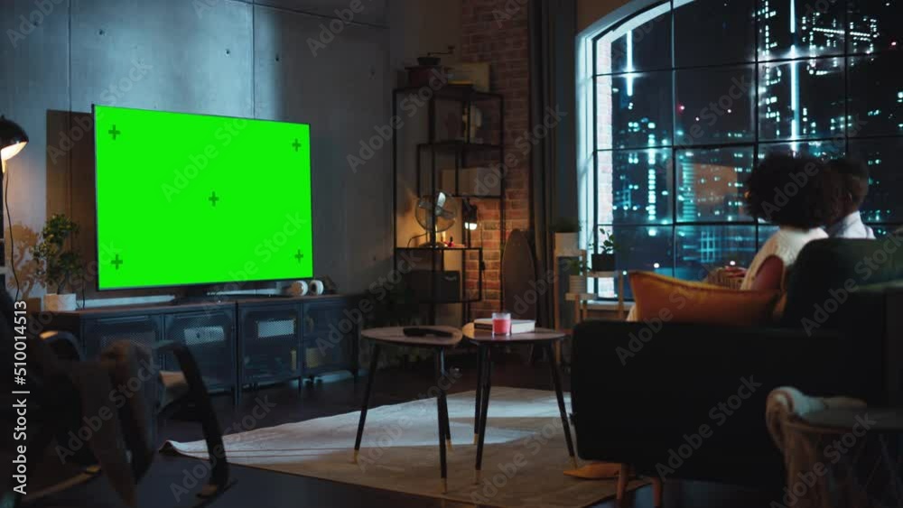 Moving Camera Shot of Black Boyfriend and Girlfriend Sitting on a Sofa in Living Room, Eating Popcorn and Watching TV with Green Screen Display. Couple Embracing and Have Pleasant Evening Moving Camera Shot of Black Boyfriend and Girlfriend Sitting on a Sofa in Living Room, Eating Popcorn and Watching TV with Green Screen Display. Couple Embracing and Have Pleasant Evening