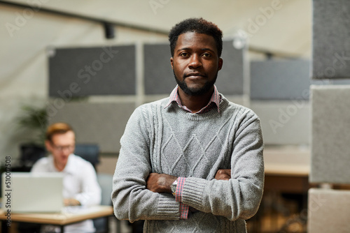 Portrait of content confident handsome black specialist with beard crossing arms on chest and standing in office of programming company