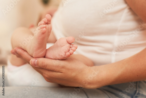 Mother feeding newborn baby girl and touching her small feet, selective focus